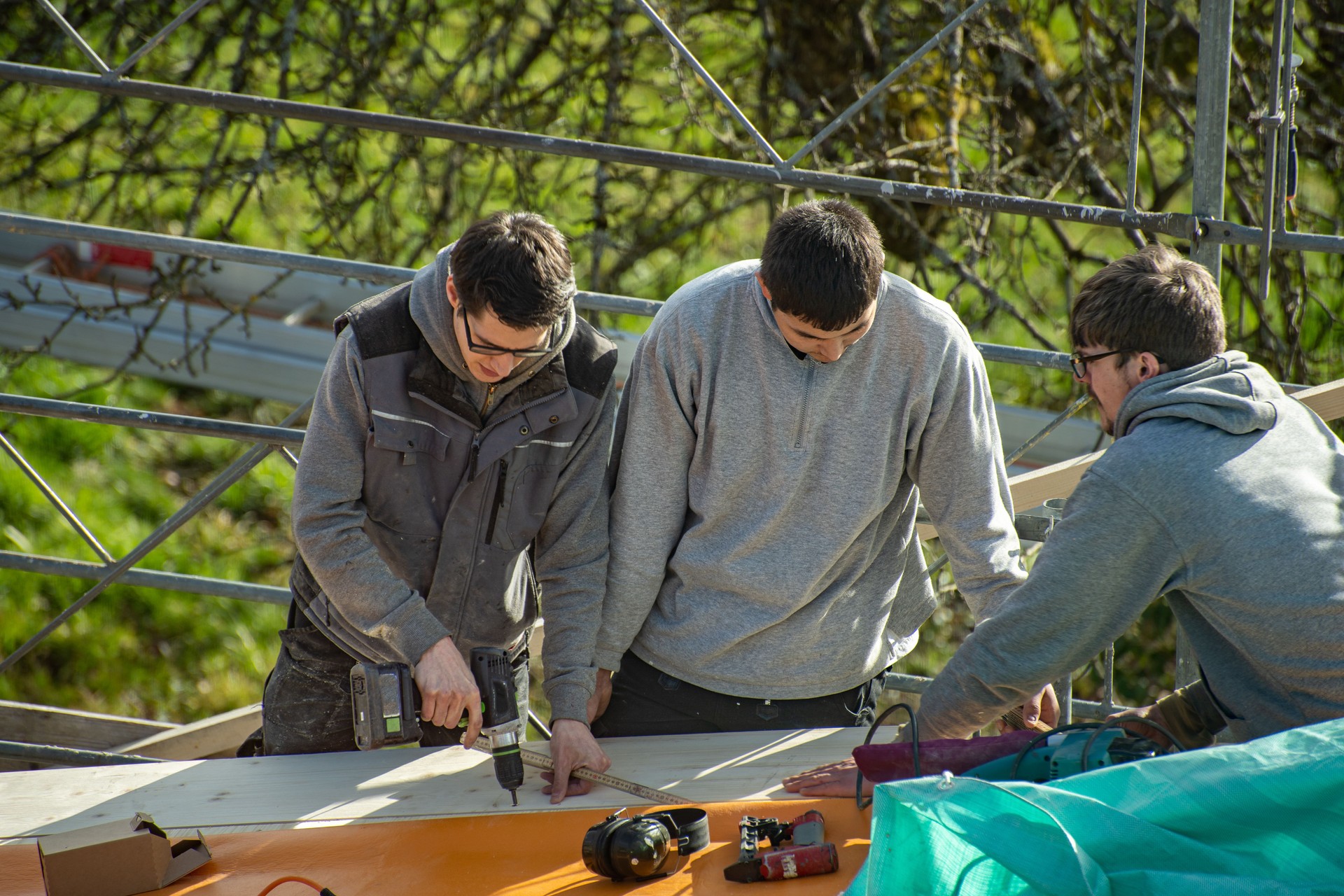 Three young carpenters working on a roof. Apprentice learns from trainer.
